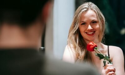 Smiling woman with a red rose in a romantic indoor setting, perfect for Valentine's celebration.